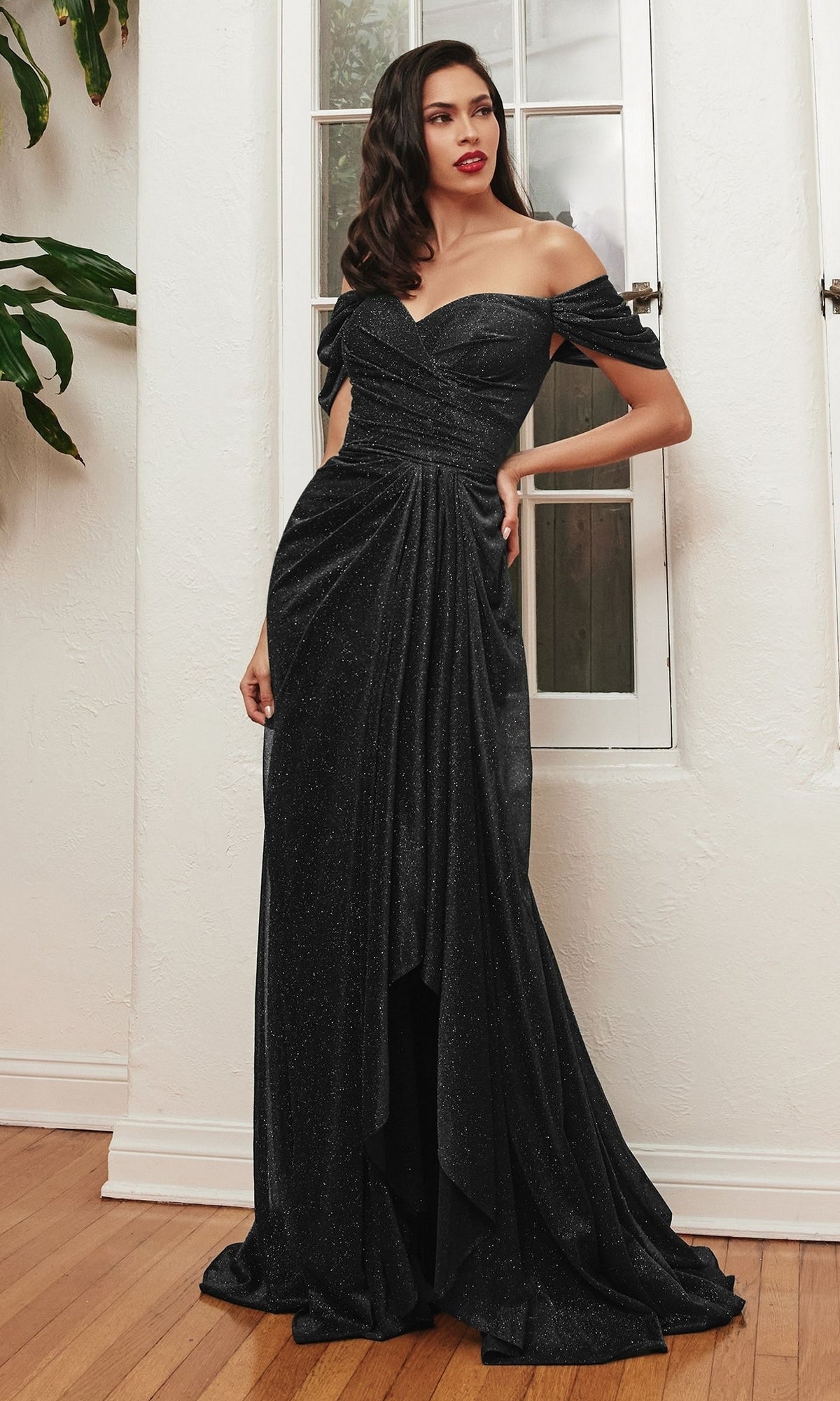 Woman wearing the Wrap-Waist Long Glitter Prom Dress CD878, featuring an off-the-shoulder design and draped floor-length skirt, stands indoors by a white wall and window—an affordable evening gown ideal for special occasions.